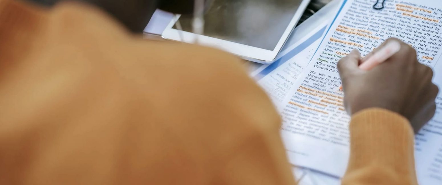 Person sitting at a desk, editing and highlighting printouts with an orange highlighter, shaping their manuscript.