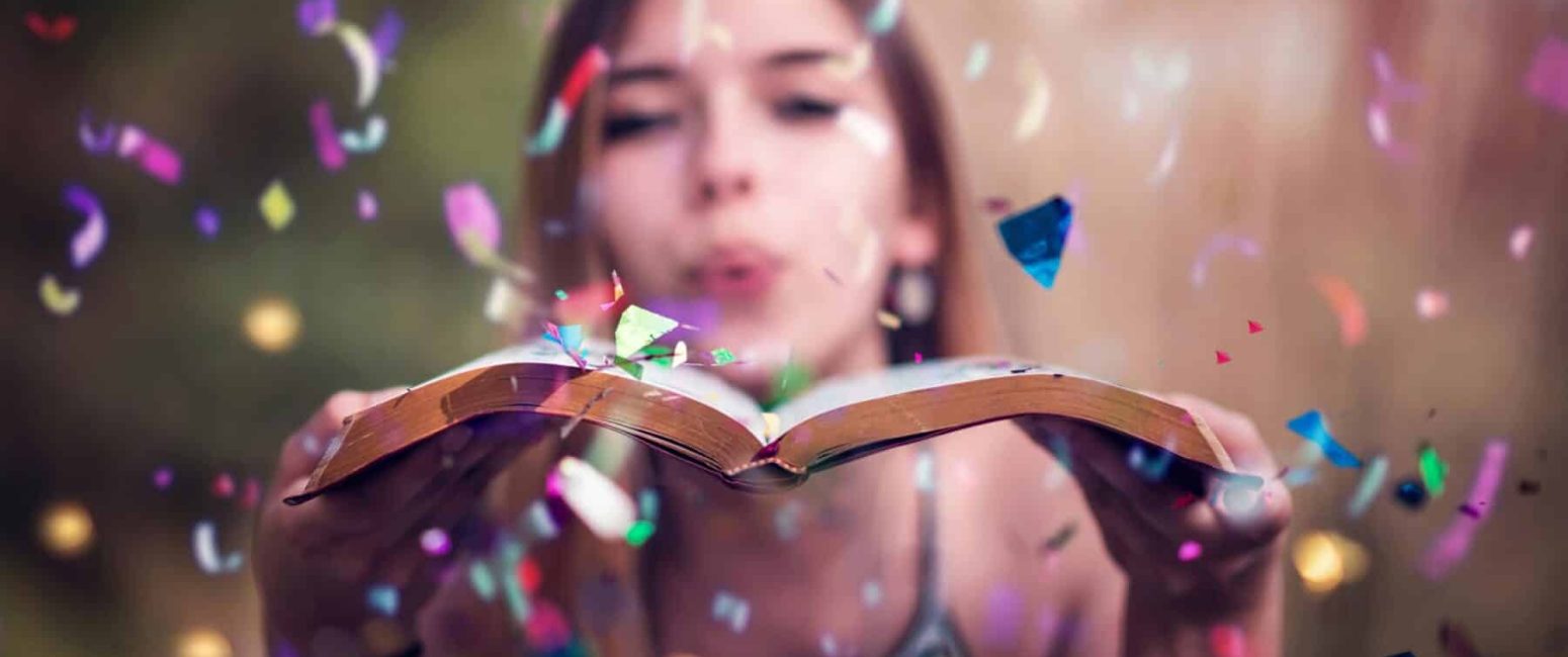 Woman blowing a kiss onto an open book in the foreground, celebrating the magic of storytelling and creativity.