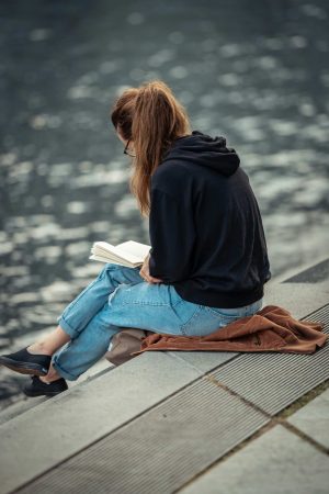 Young woman reading a book by the water, immersed in a world of ideas